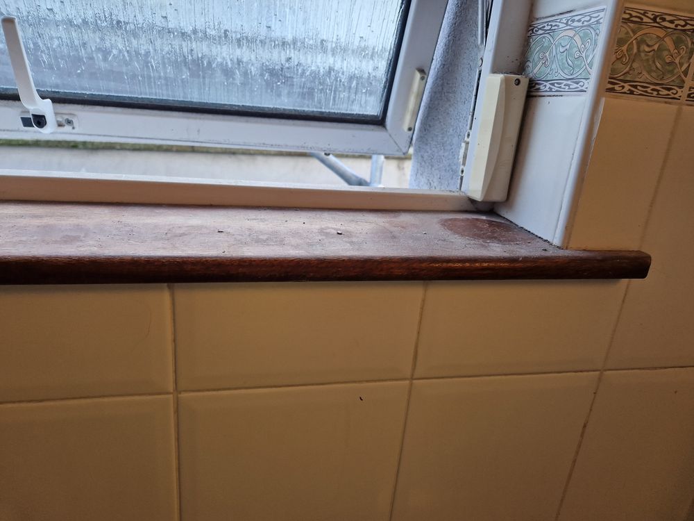 Bathroom window sill before cleaning, with water marks and dust on the wood