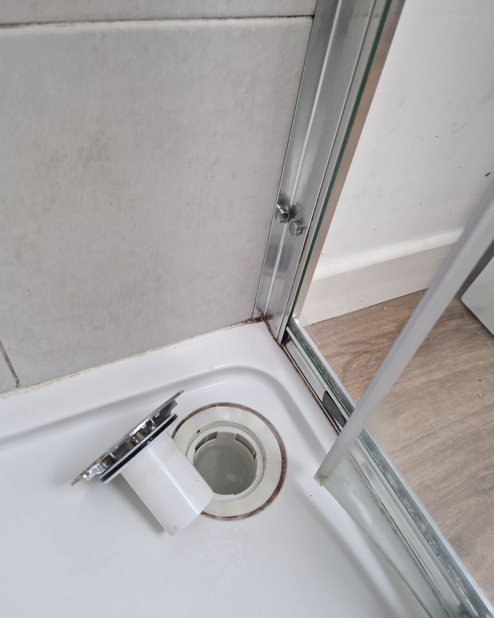 The same shower tray after cleaning, with the drain cover lifted and the track clean