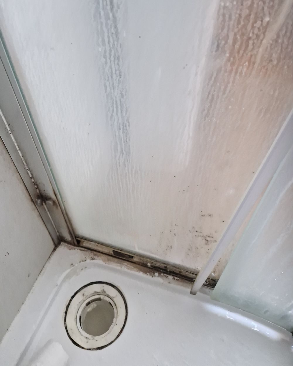 Shower tray before cleaning, with mould and black grime along the door track
